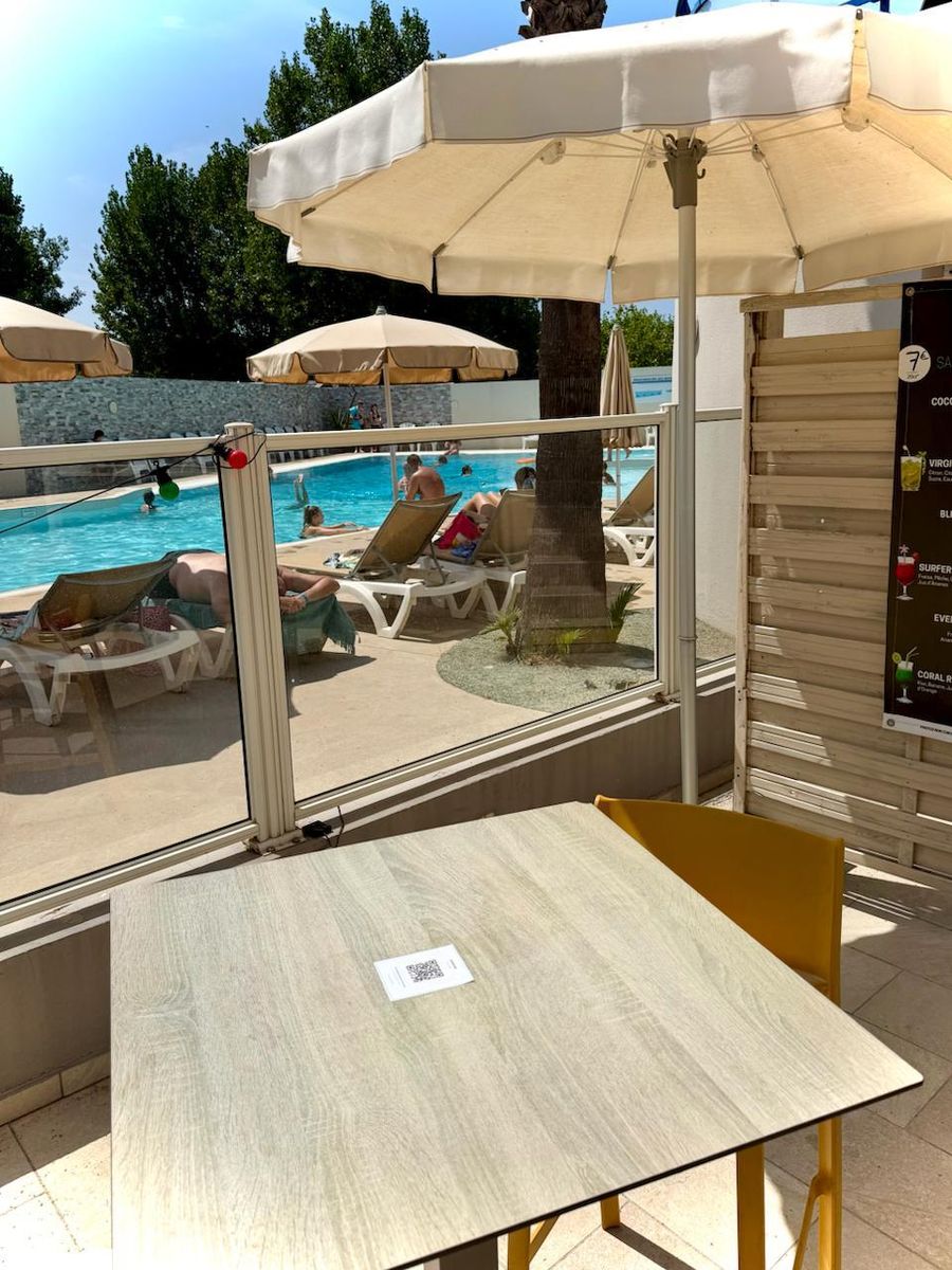 Une table de la terrasse du Bonap, au bord de la piscine, avec son QR code de menu posé au centre