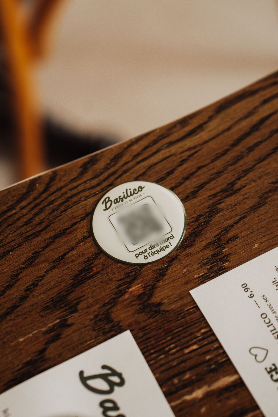 Une pastille ronde Basilico posée sur une table en bois, avec un QR code et la phrase « pour dire merci à l'équipe ! »